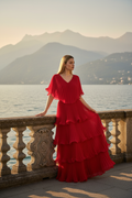 Model wearing Astra red evening gown with V-neck and tiered pleated chiffon skirt